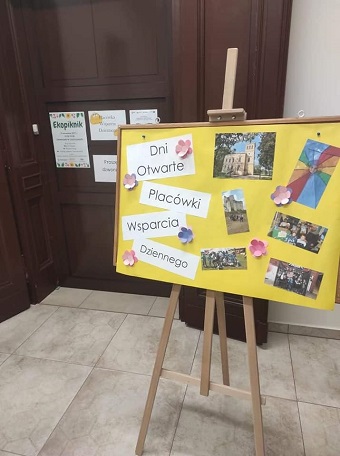 Na zdjęciu żółta tablica korkowa, na której są zdjęcia z dziećmi z Placówki Wsparcia Dziennego z Leszczyn oraz informacja o Dni Otwartych Placówki Wsparcia Dziennego