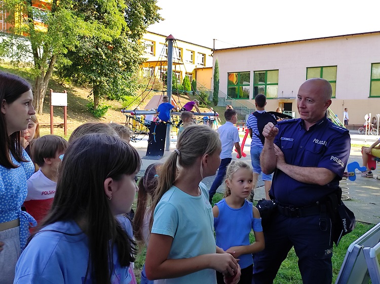 Na zdjęciu dzielnicowy asp. Marcin Bogacz informujący dzieci o zasadach bezpiecznego poruszania się po drodze